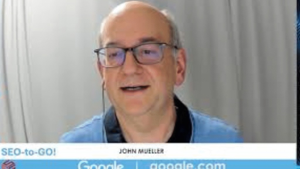 a picture of John Mueller in a zoom meeting. He is wearing a ligh colored blue shirt with black collar and pair of reading glasses.